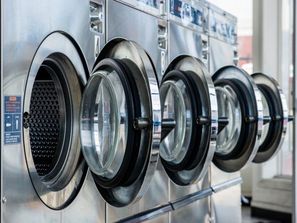 Modern on-site laundry room at Linden Village featuring rows of high-capacity stainless steel washing machines.