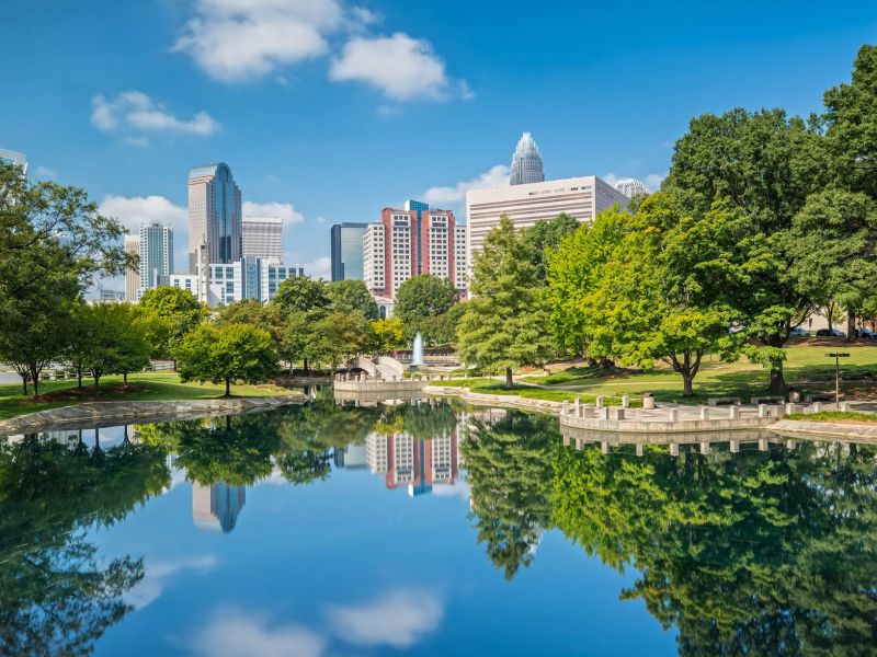 Scenic view of downtown Charlotte near Linden Village with city skyline reflected in a peaceful park pond.